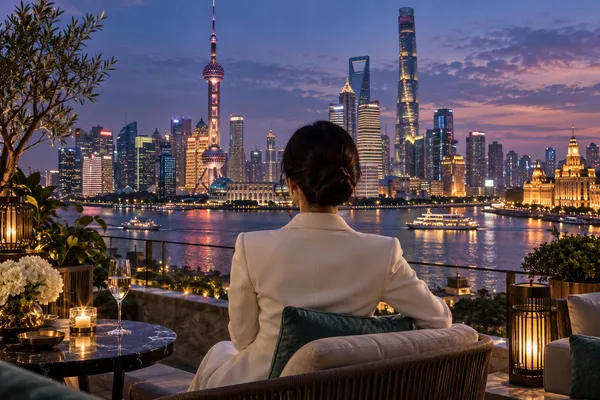 An adult woman in an ivory jacket looking across a Shanghai-inspired river skyline at dusk